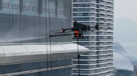 Drone with a Pliabot payload flying next to a glass tower