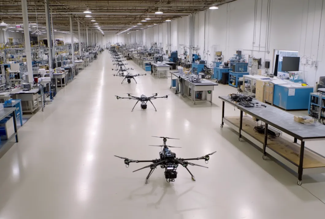 Long assembly hall with test benches and several multirotor drones on the floor
