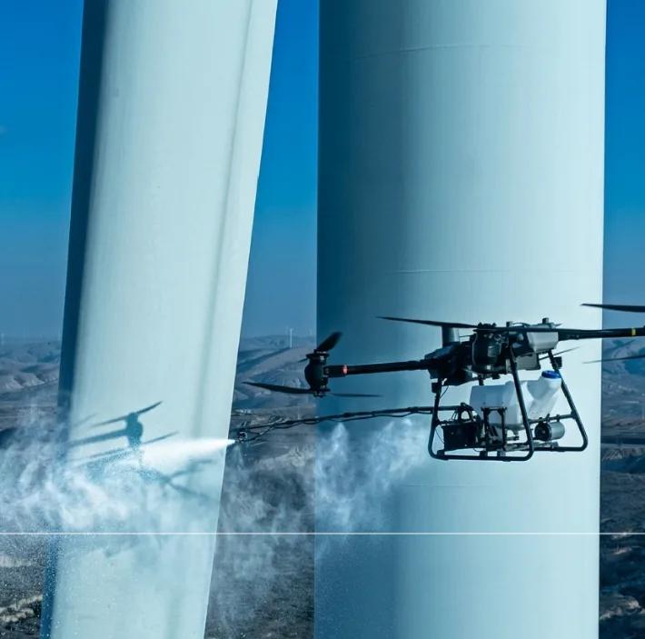 Cleaning drone spraying a wind turbine tower above the clouds